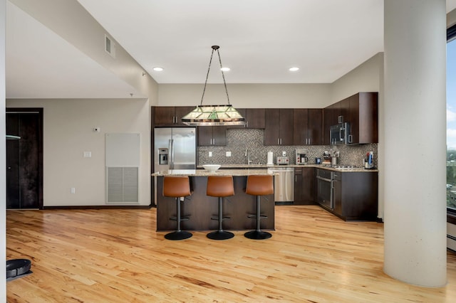 1240 2nd St Unit 701, Minneapolis, MN 55415 - kitchen featuring stainless steel appliances, a breakfast bar, dark brown cabinetry, light wood finished floors, and backsplash