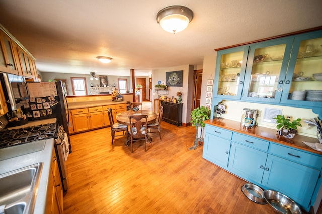 kitchen with light wood-style floors, glass insert cabinets, stainless steel range with gas cooktop, and a sink
