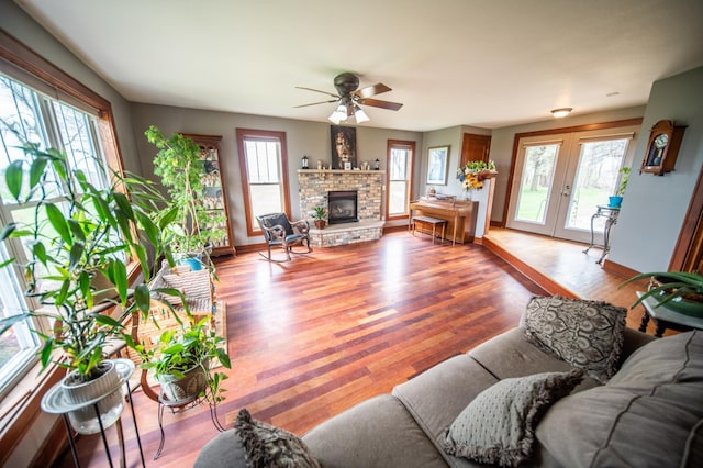 living area featuring ceiling fan, french doors, a fireplace, wood finished floors, and baseboards