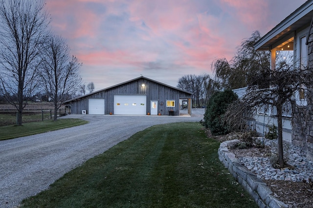 property exterior at dusk with a garage, an outbuilding, a yard, and driveway