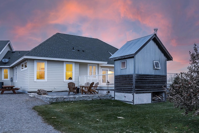 back of house at dusk with a patio, a shingled roof, and a yard