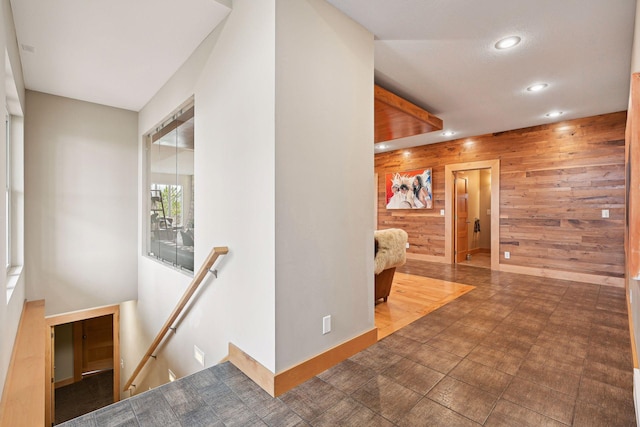 hall featuring recessed lighting, wood walls, and an upstairs landing