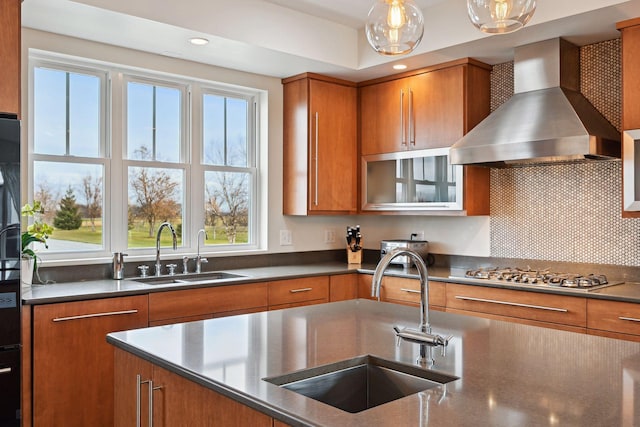 kitchen with a sink, stainless steel gas cooktop, wall chimney range hood, and brown cabinets