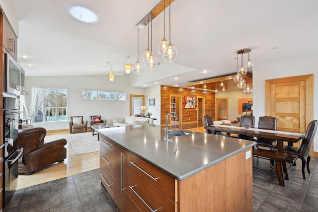 kitchen featuring stainless steel microwave, open floor plan, a sink, and a kitchen island with sink