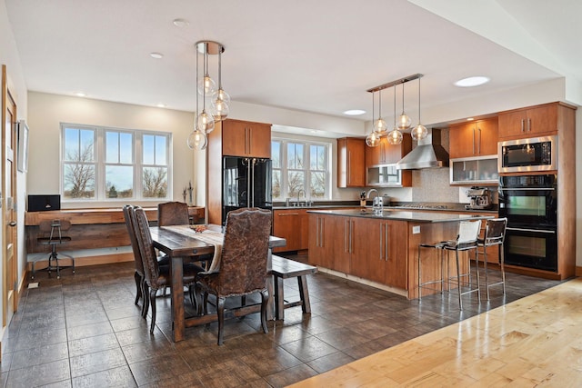 kitchen with a sink, black appliances, brown cabinets, and wall chimney exhaust hood
