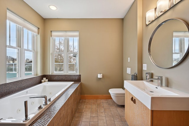 bathroom featuring toilet, baseboards, a tub with jets, and vanity