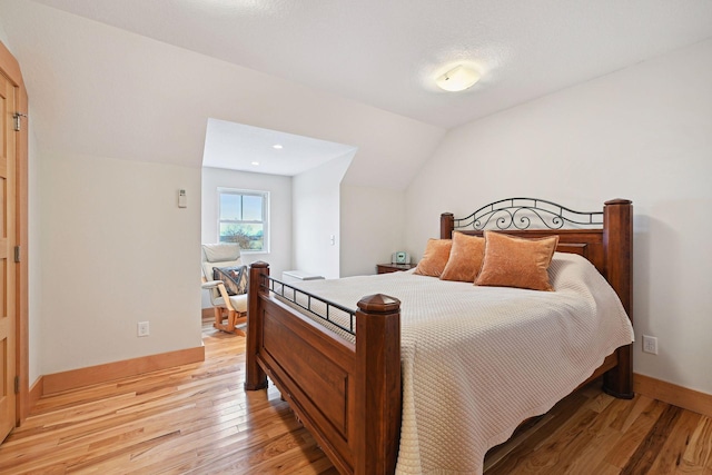 bedroom featuring light wood-style floors, baseboards, and lofted ceiling