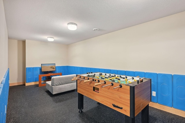 recreation room featuring a textured ceiling and wainscoting