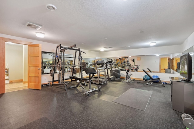 exercise room with visible vents, a textured ceiling, and baseboards