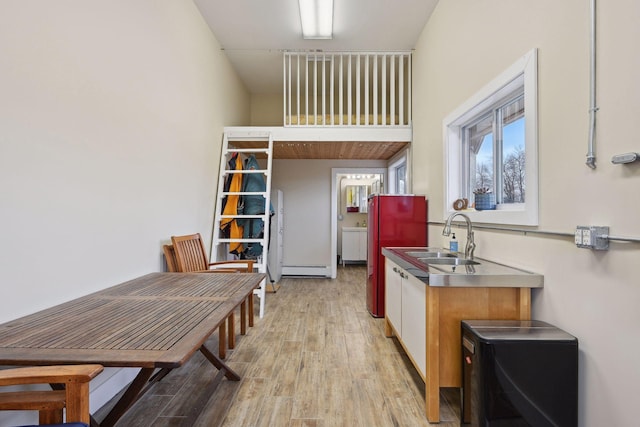kitchen featuring a sink, stainless steel counters, a baseboard radiator, and light wood-type flooring