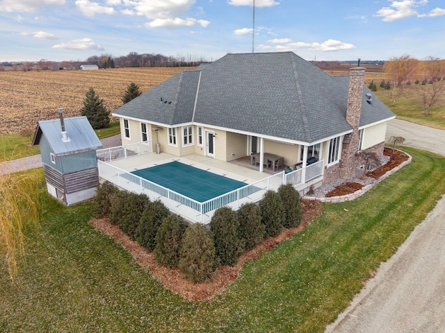 back of property featuring fence, roof with shingles, a chimney, a fenced in pool, and a lawn