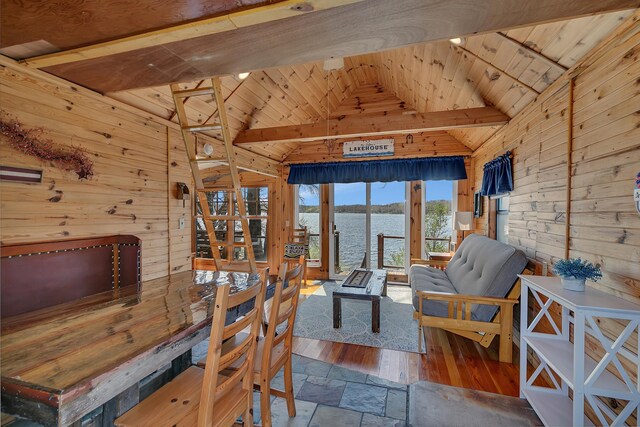 dining area featuring stone tile floors, wooden walls, wood ceiling, a water view, and lofted ceiling with beams