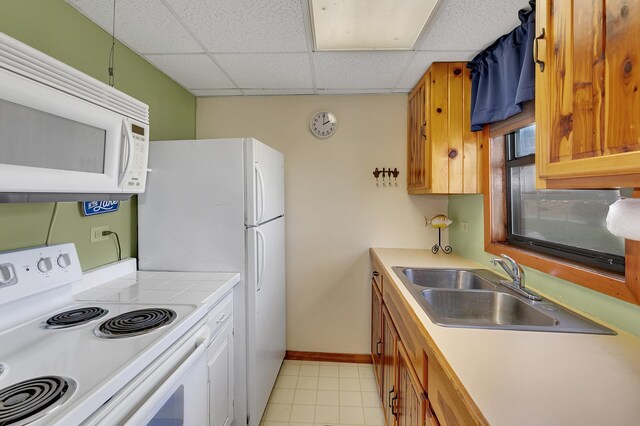 kitchen with white appliances, baseboards, a paneled ceiling, a sink, and light tile patterned floors