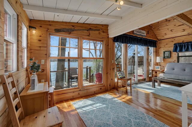living area with a water view, hardwood / wood-style flooring, lofted ceiling with beams, and wood walls