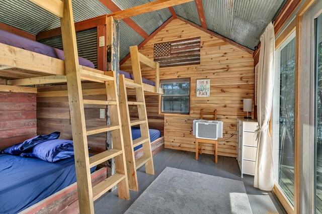 bedroom with wooden walls, multiple windows, wood finished floors, and lofted ceiling