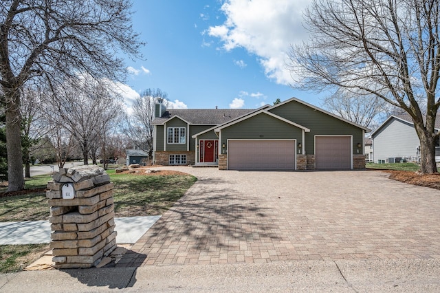 view of front facade with decorative driveway, a chimney, an attached garage, and stone siding