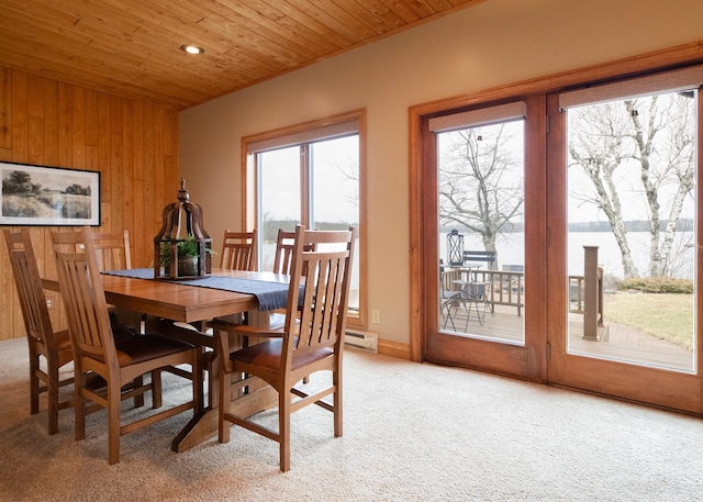 dining space featuring a baseboard heating unit, wooden ceiling, wood walls, and light colored carpet