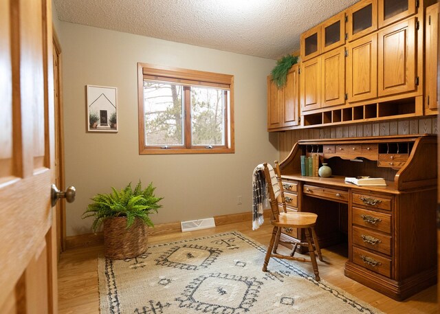 office space featuring baseboards, visible vents, a textured ceiling, and light wood-style floors
