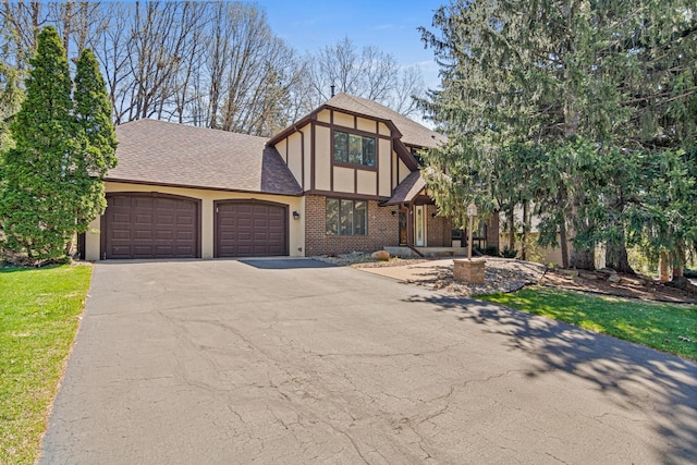 english style home with roof with shingles, an attached garage, driveway, and brick siding
