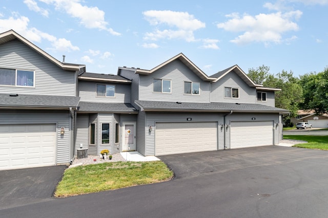 multi unit property featuring central AC unit, driveway, a shingled roof, and a garage