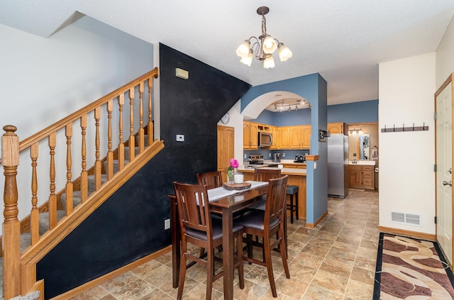 dining area featuring stone finish floor, visible vents, arched walkways, baseboards, and a chandelier