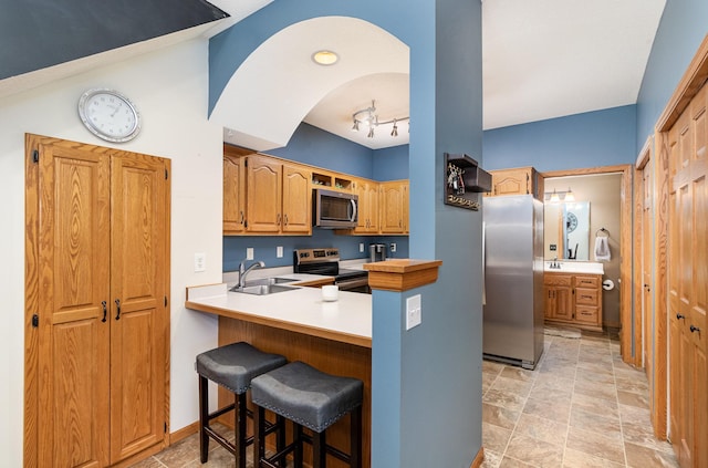 kitchen with stainless steel appliances, a peninsula, light countertops, a sink, and a breakfast bar