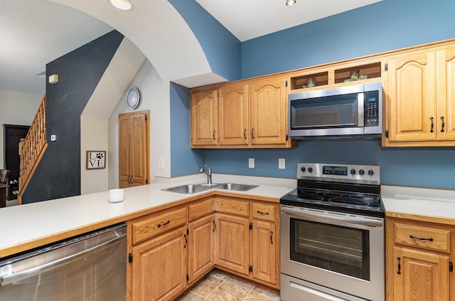 kitchen with light countertops, a sink, arched walkways, a peninsula, and appliances with stainless steel finishes