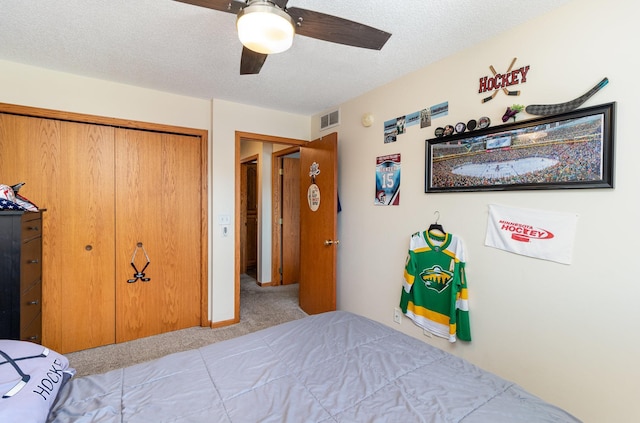 bedroom with a textured ceiling, visible vents, a ceiling fan, a closet, and carpet floors