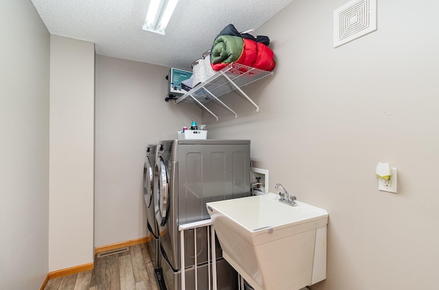 clothes washing area with wood finished floors, a sink, laundry area, visible vents, and independent washer and dryer