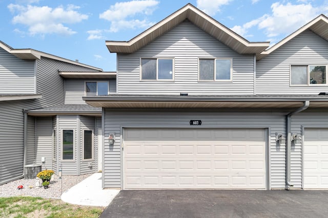 view of property with an attached garage, aphalt driveway, and central air condition unit