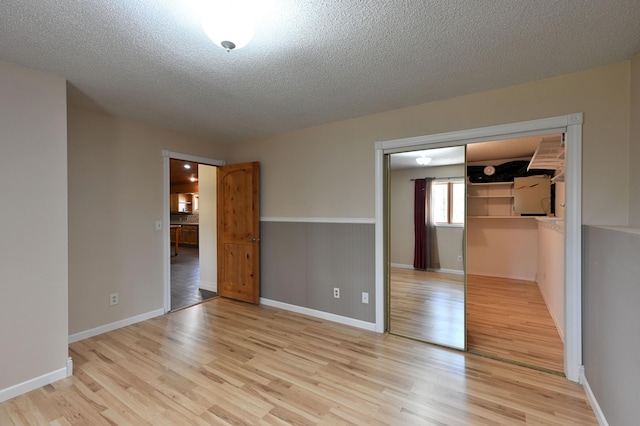 unfurnished bedroom featuring a textured ceiling, light wood-style flooring, and baseboards