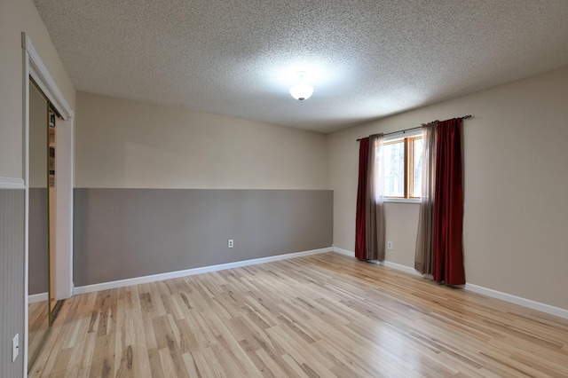 unfurnished room with a textured ceiling, light wood-type flooring, and baseboards