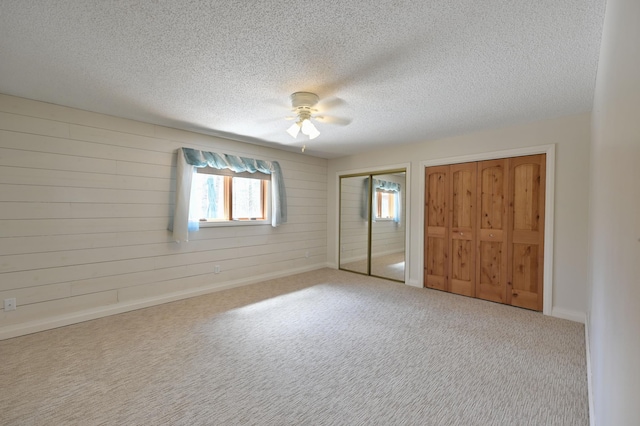 unfurnished bedroom featuring a textured ceiling, carpet floors, wooden walls, multiple closets, and a ceiling fan