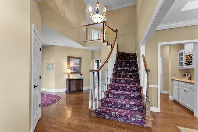 staircase featuring baseboards, ornamental molding, wood finished floors, and a high ceiling