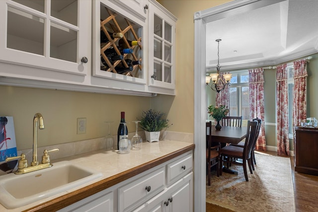 bar with dark wood-type flooring, a sink, a tray ceiling, and a notable chandelier