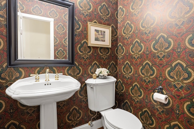 bathroom with toilet, wallpapered walls, and baseboards