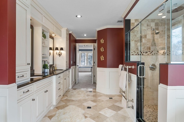 full bath featuring vanity, ornamental molding, wainscoting, visible vents, and a stall shower