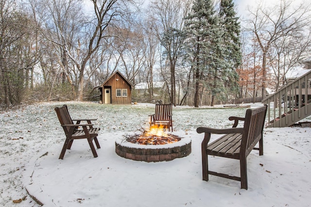 snow covered patio featuring a storage shed, an outbuilding, and an outdoor fire pit