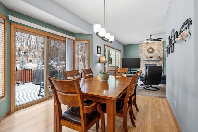 dining space with light wood finished floors, a ceiling fan, baseboards, and a fireplace