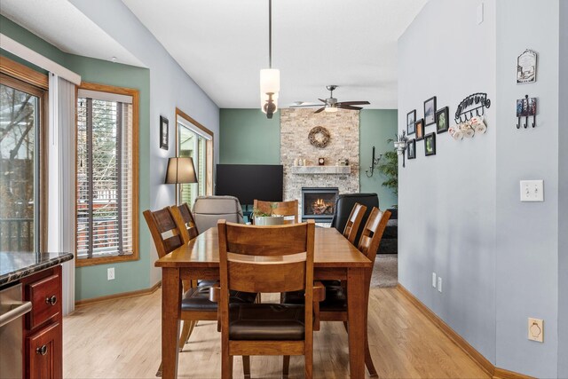 dining area featuring light wood-type flooring, a stone fireplace, and a healthy amount of sunlight