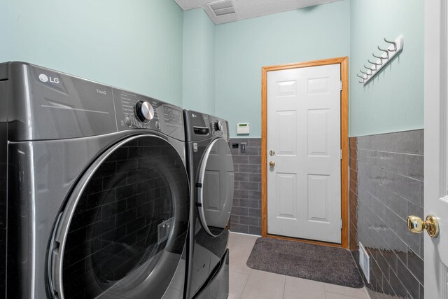 laundry area with tile patterned floors, separate washer and dryer, visible vents, tile walls, and wainscoting