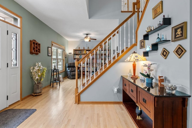 foyer entrance with baseboards, a ceiling fan, wood finished floors, and stairway