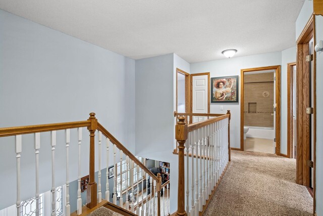 corridor featuring carpet floors, baseboards, and an upstairs landing