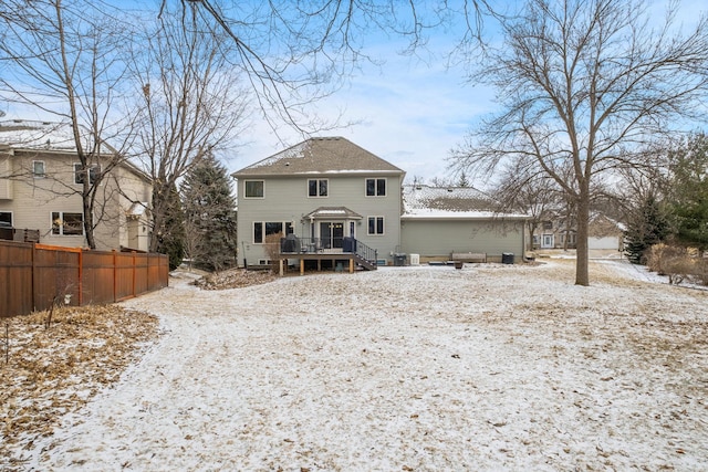 snow covered rear of property with a wooden deck and fence
