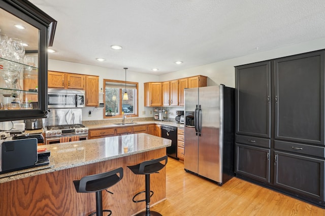 kitchen featuring a kitchen bar, appliances with stainless steel finishes, a sink, light stone counters, and light wood finished floors