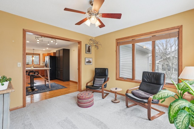 living area featuring a ceiling fan, baseboards, and light carpet