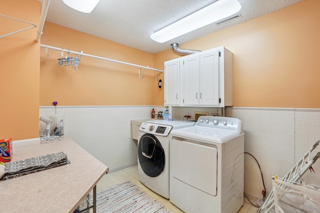 laundry area featuring cabinet space, visible vents, wainscoting, and washer and clothes dryer