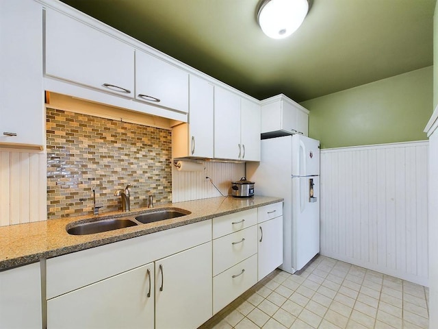 kitchen with backsplash, wainscoting, a sink, white cabinets, and freestanding refrigerator