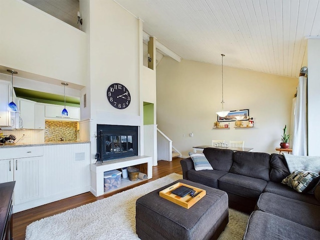 living room featuring high vaulted ceiling, a glass covered fireplace, stairway, and dark wood-type flooring
