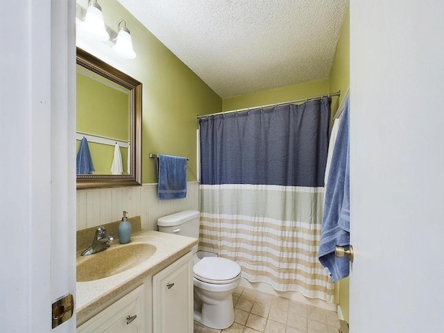 bathroom with a textured ceiling, wainscoting, vanity, tile patterned floors, and toilet